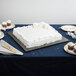 An 18" white square cake drum under a white frosted cake on a table.