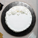 A white cake with white frosting on a black Enjay round cake drum.