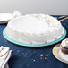 A white cake on a blue Enjay round cake drum on a table with a napkin, fork, and knife.