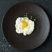 A black Oneida Lava porcelain plate with a fried egg on it.