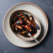 An oval porcelain bowl filled with mussels in sauce with a fork.