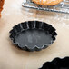 A black fluted Matfer Bourgeat tartlet mold on a counter.