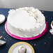 An Enjay pink round cake drum under a white cake on a table.