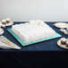 A white square cake with blue frosting on a table with plates and a fork.