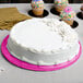 A white cake with pink frosting on a pink Enjay cake drum on a table.