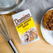 A cinnamon roll on a plate next to a box of Domino Dark Brown Sugar.