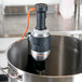 A KitchenAid immersion blender with a cord attached in a pot.
