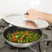 A hand holding a Vollrath Torogard lid over a pan of vegetables.