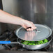 A person holding a Vollrath Torogard lid over a pot of broccoli.