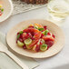 A Bamboo by EcoChoice round bamboo plate with fruit salad and a wooden fork.
