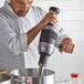 A chef using a KitchenAid 400 Series immersion blender in a metal pot.