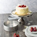 A cake with strawberries on top of it on a plate next to a Chicago Metallic Springform Cake Pan.