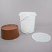 A white plastic bucket with a brown base and tap.