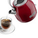 A red KitchenAid electric kettle pouring liquid into a glass cup.