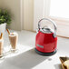 A red KitchenAid electric kettle on a counter next to two cups of chocolate milk.
