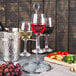 A Franmara metal stand holding three wine glasses filled with red and white wine on a table with a bottle of wine.