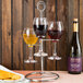 A Franmara steel wine flight rack holding three glasses of wine on a metal stand with crackers on a table.