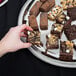 A hand holding a brownie on a Vollrath stainless steel serving tray.