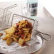 An American Metalcraft stainless steel mini square fry basket on a plate of fries.