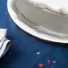 A white cake on a silver round cake drum on a blue table.