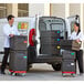 A man and woman loading Cambro black top loading EPP insulated food pan carriers into a van.