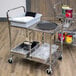 A Luxor wire utility cart with food containers and pans on it.