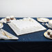 A white cake on a silver square cake drum on a blue table.