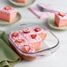 A pink cake with strawberries in a clear glass square cake dish.