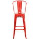 A red metal bar stool with a vertical slat back and drain hole seat.