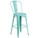 A green metal bar stool with a backrest and drain hole seat.