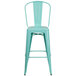 A green metal bar stool with a backrest and a white seat with a hole in it.