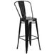 A Flash Furniture black galvanized steel bar stool with a vertical slat back and drain hole seat.