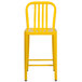 A yellow metal indoor/outdoor counter height stool with a vertical slat back.