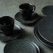 A stack of black Oneida Urban porcelain pedestal bowls on a table.