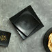 A black Oneida Urban curved square porcelain plate with food on it.