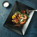 A black rectangular Oneida Urban sushi plate with shrimp and vegetables on it.