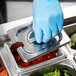 A person wearing blue gloves using a Vollrath stainless steel steam table pan cover to serve food.