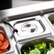 A Vollrath stainless steel slotted hotel pan cover on a counter with a tray of food.