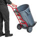 A person using a Rubbermaid construction and landscape trash can dolly to move a large grey trash can.