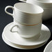 A stack of Oneida Manhattan warm white porcelain cups and saucers.