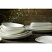 A stack of Oneida warm white porcelain oval soup bowls on a wooden table.