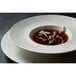A white Oneida porcelain rim soup bowl with a plate of soup with mushrooms in it.