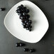 A Oneida warm white porcelain plate with black grapes on a table.