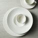 A stack of Oneida Manhattan warm white porcelain wide rim coupe plates.