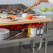 A chef using a Regency stainless steel plate shelf on a long kitchen counter.