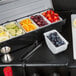 A tray of fruit and berries on a counter with a Choice condiment dispenser insert holding a container of strawberries.