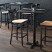 A Lancaster Table & Seating black cross back bar stool with a natural wood seat on a table in a restaurant.