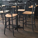 A Lancaster Table & Seating black cross back bar stool with a natural wood seat at a table in a restaurant