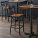 A Lancaster Table & Seating black cross back bar stool with a wooden seat next to a table.