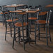 A Lancaster Table & Seating black cross back bar stool with an antique walnut wood seat on a table in a restaurant.